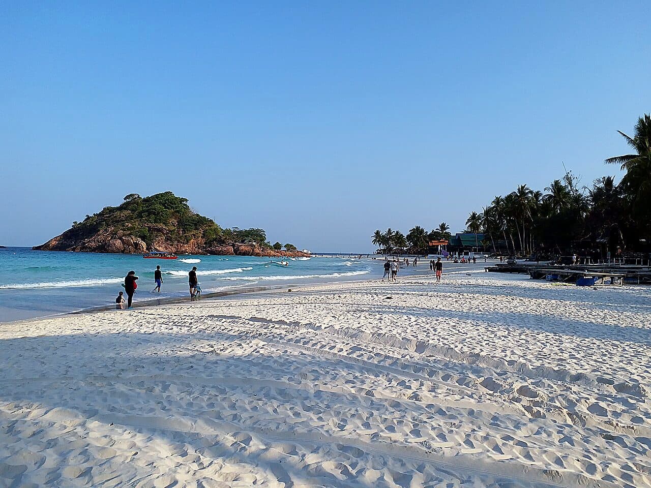 White sand and clear shallows on Long Beach (Pasir Panjang), Pulau Redang, with the rocky islet offshore and resorts along the bay