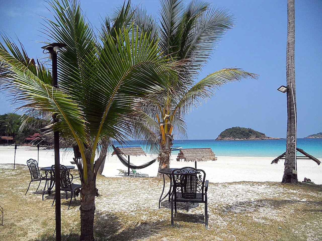 A Pulau Redang resort beachfront — palms, hammocks and shaded tables on the sand, with the beach and a headland beyond